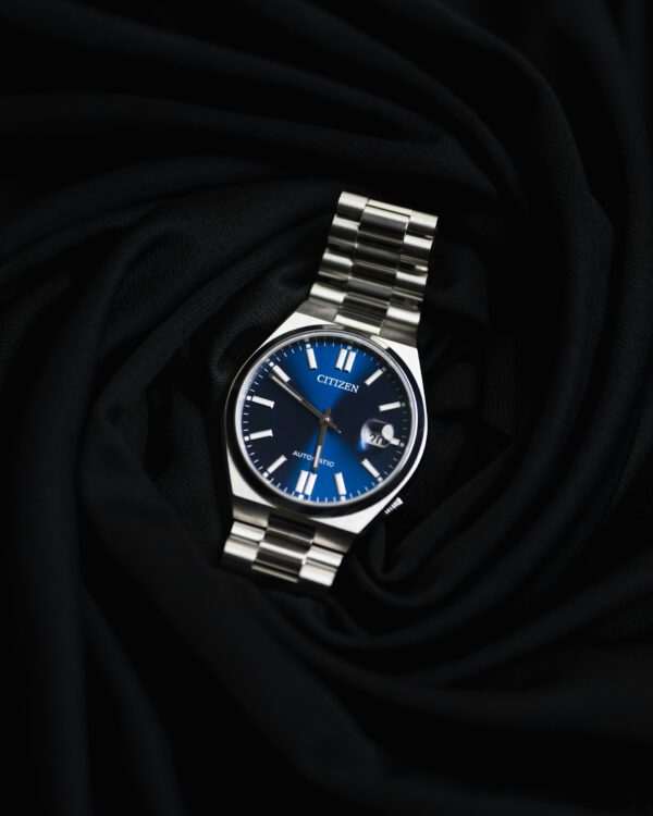 Zilver met blauw analoog automatisch rond Citizen horloge met datumaanduiding op zwarte stoffen ondergrond.