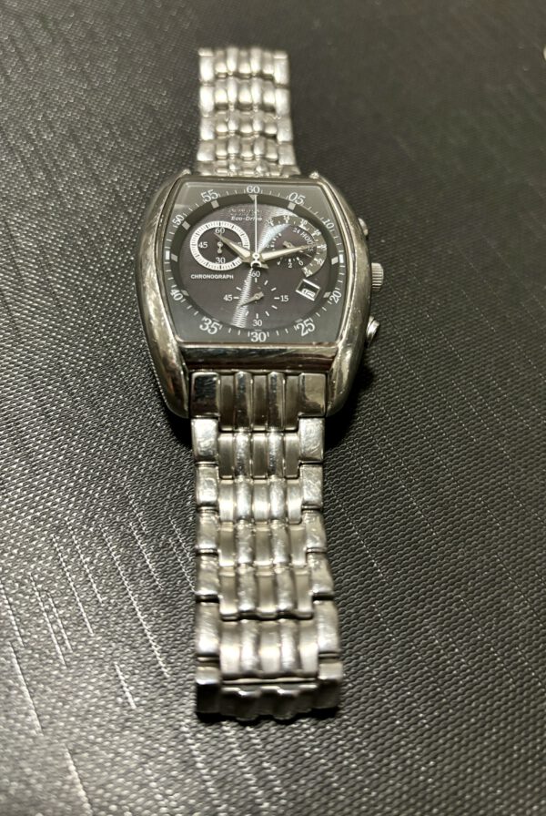 Zilver en grijs horloge met witte wijzers en datum aanduiding op zwarte ondergrond.