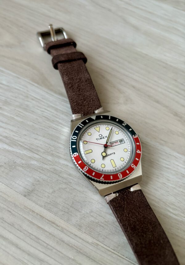 Blauw met rood en wit analoog quartz rond Timex horloge met lederen band op houten ondergrond.